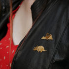 Pins dinosaure et pins tricératops finition or portés sur une veste en cuir - Les Naturalistes bijoux